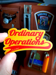 Ordinary operations sticker, red on yellow. By TJ Leather. Held by hand